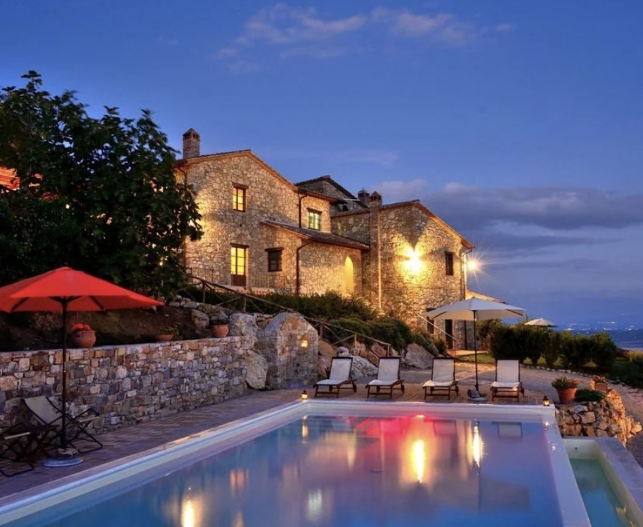 Farmhouse Fontanelle lit up at dusk beside its pool
