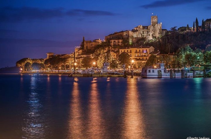 Passignano sul Trasimeno at night, its castle and waterfront lit up and reflected in the lake